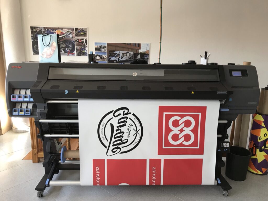 Máquina de impresión a gran formato produciendo vinilos personalizados con acabados profesionales, ideal para rótulos, decoración, publicidad y proyectos de diseño gráfico para empresas.